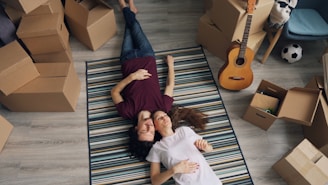 a man and woman laying on a rug in a room full of moving boxes