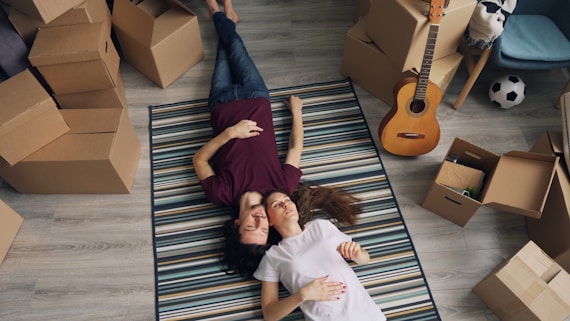 a man and woman laying on a rug in a room full of moving boxes