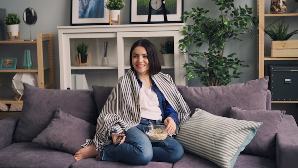 a woman sitting on a couch holding a bowl of popcorn