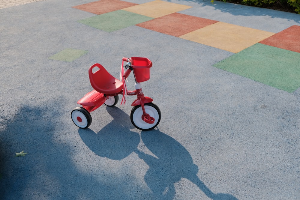 a red tricycle sitting on top of a sidewalk