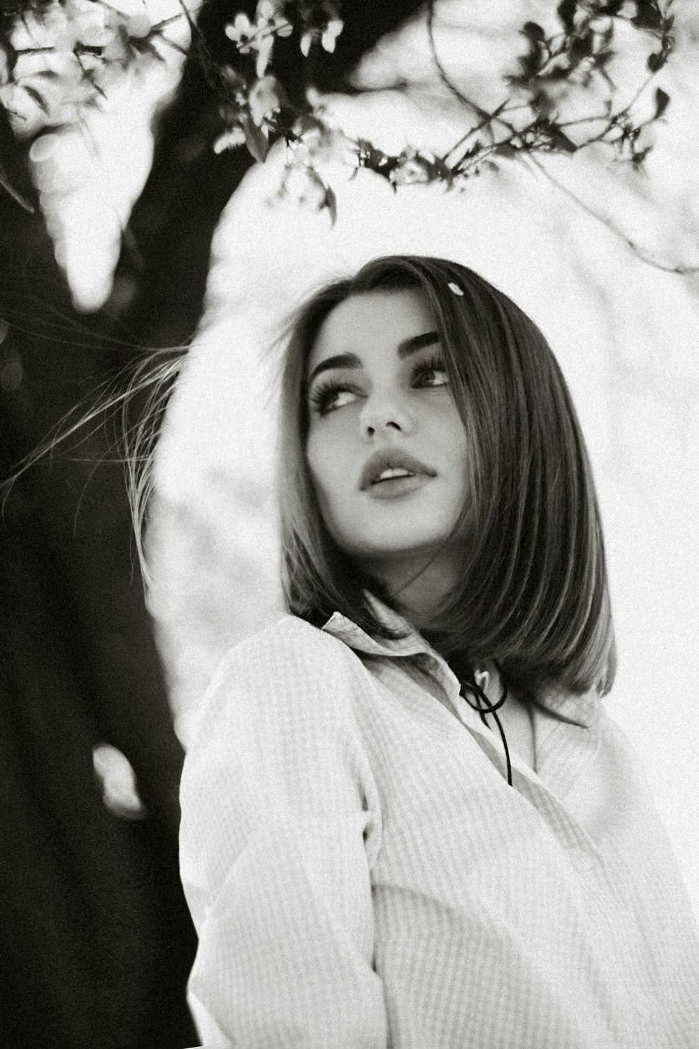 a black and white photo of a woman leaning against a tree