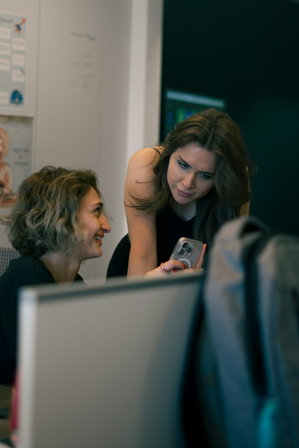 a woman looking at a cell phone while sitting in front of a laptop