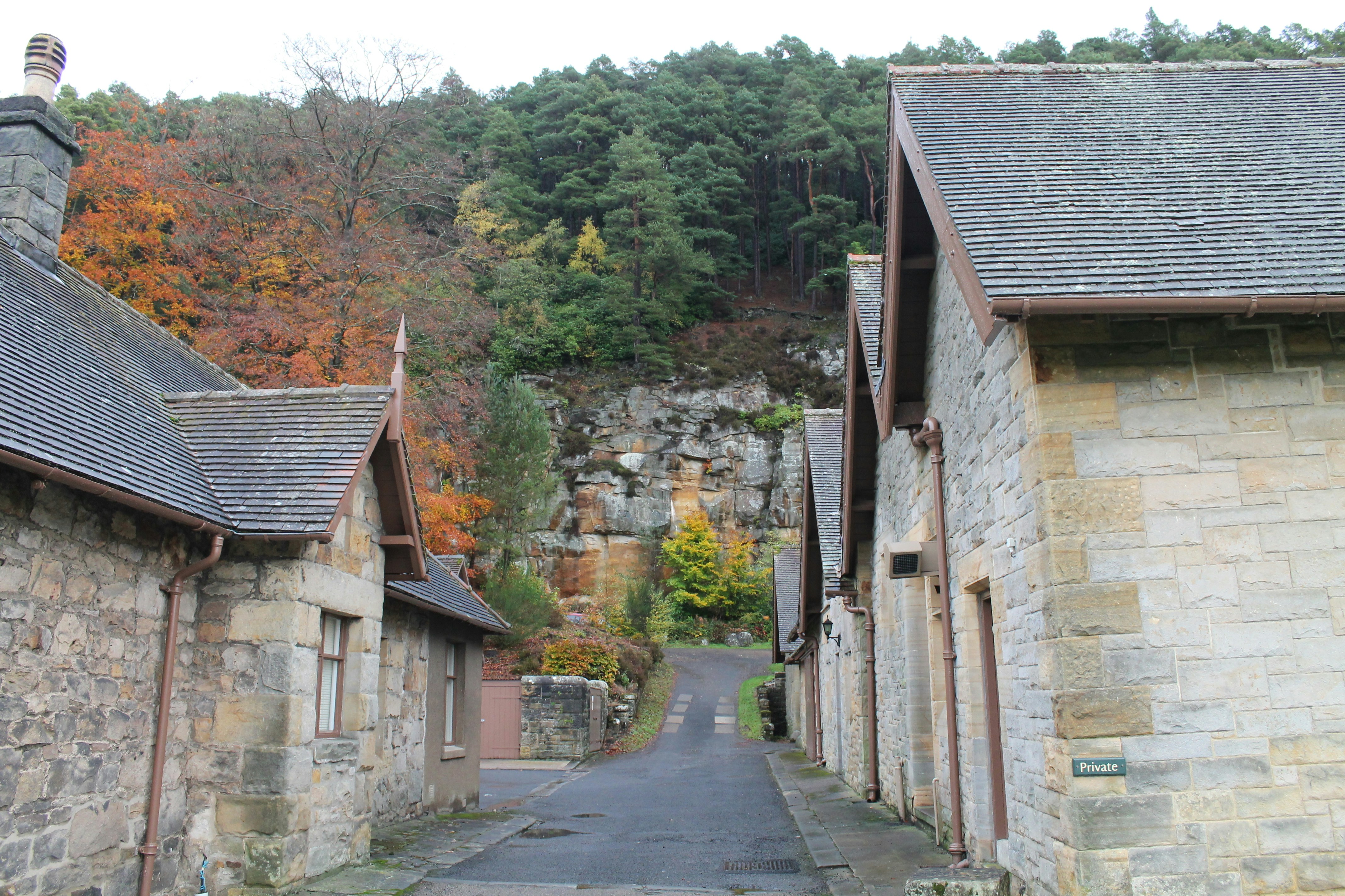 a narrow road between two stone buildings with a steep cliff in the background