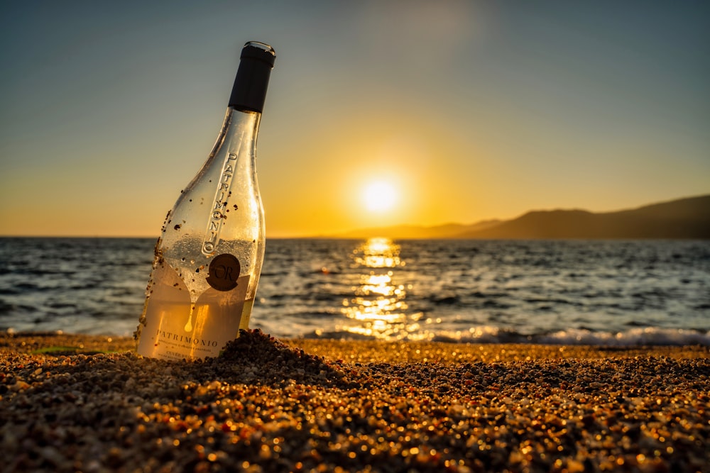 a bottle of wine sitting on top of a sandy beach