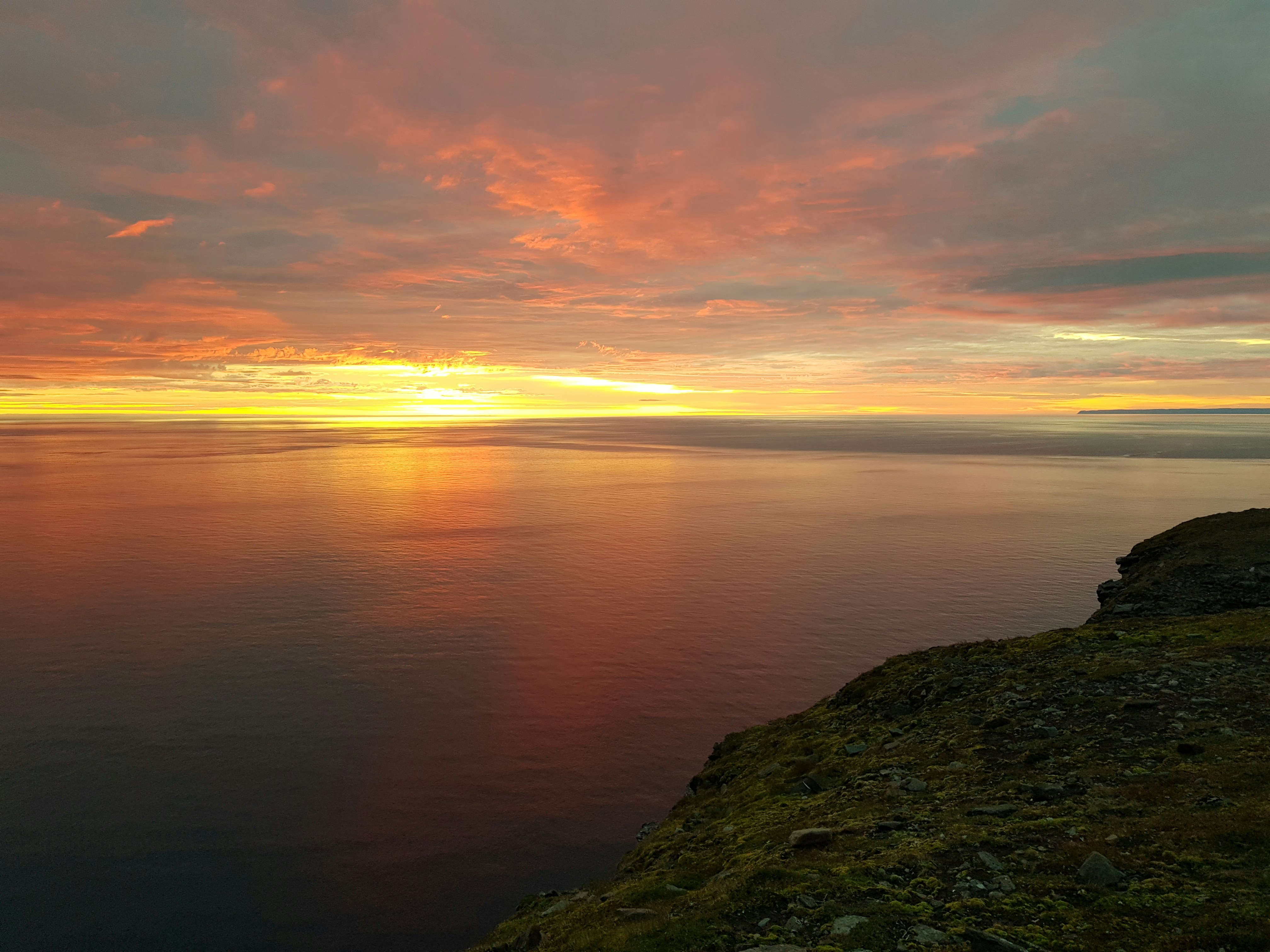 a sunset over a body of water with a hill in the foreground