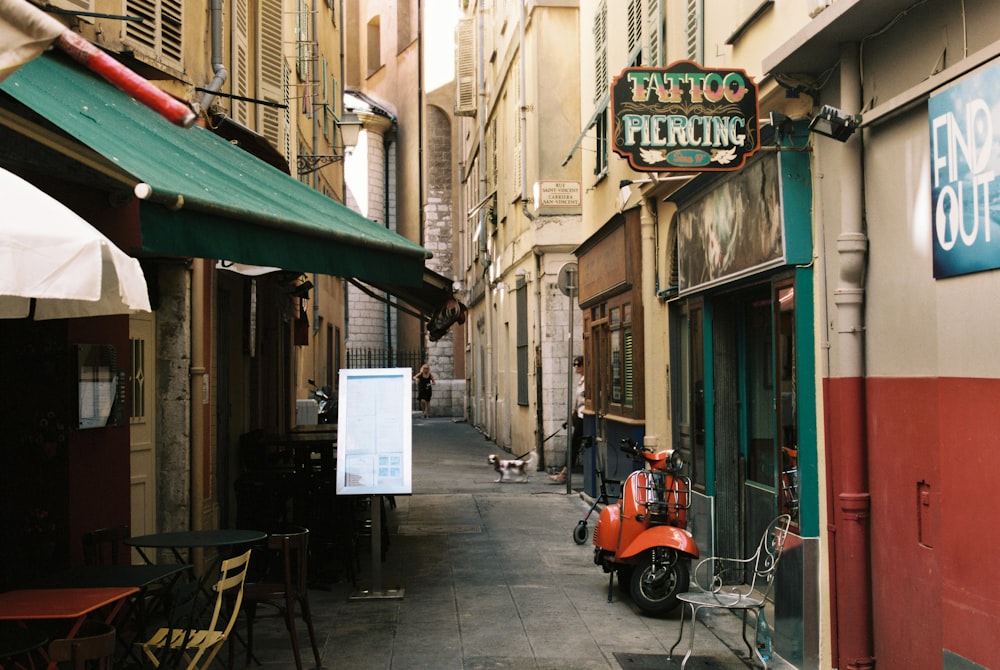 a narrow street with tables and chairs and a scooter parked in front of