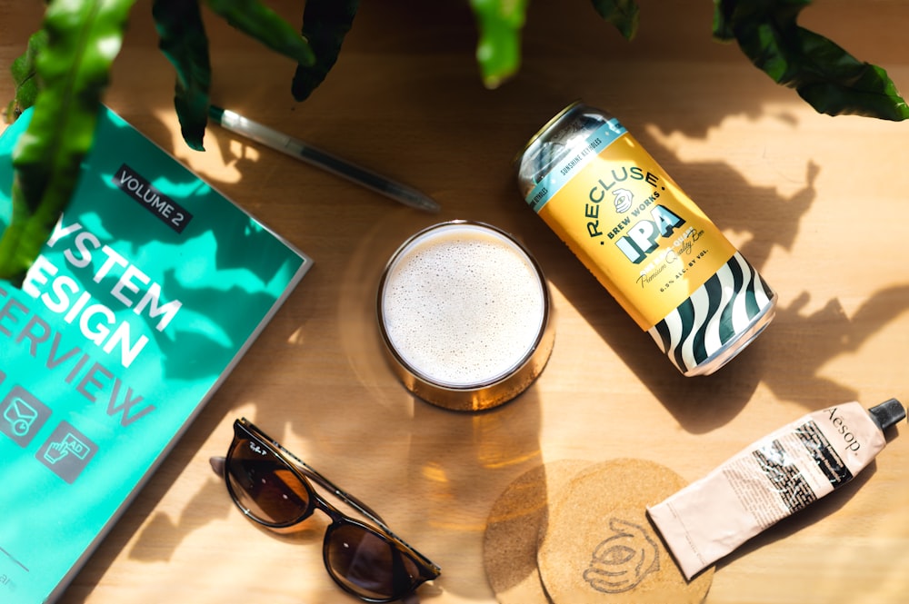a wooden table topped with a can of beer and sunglasses