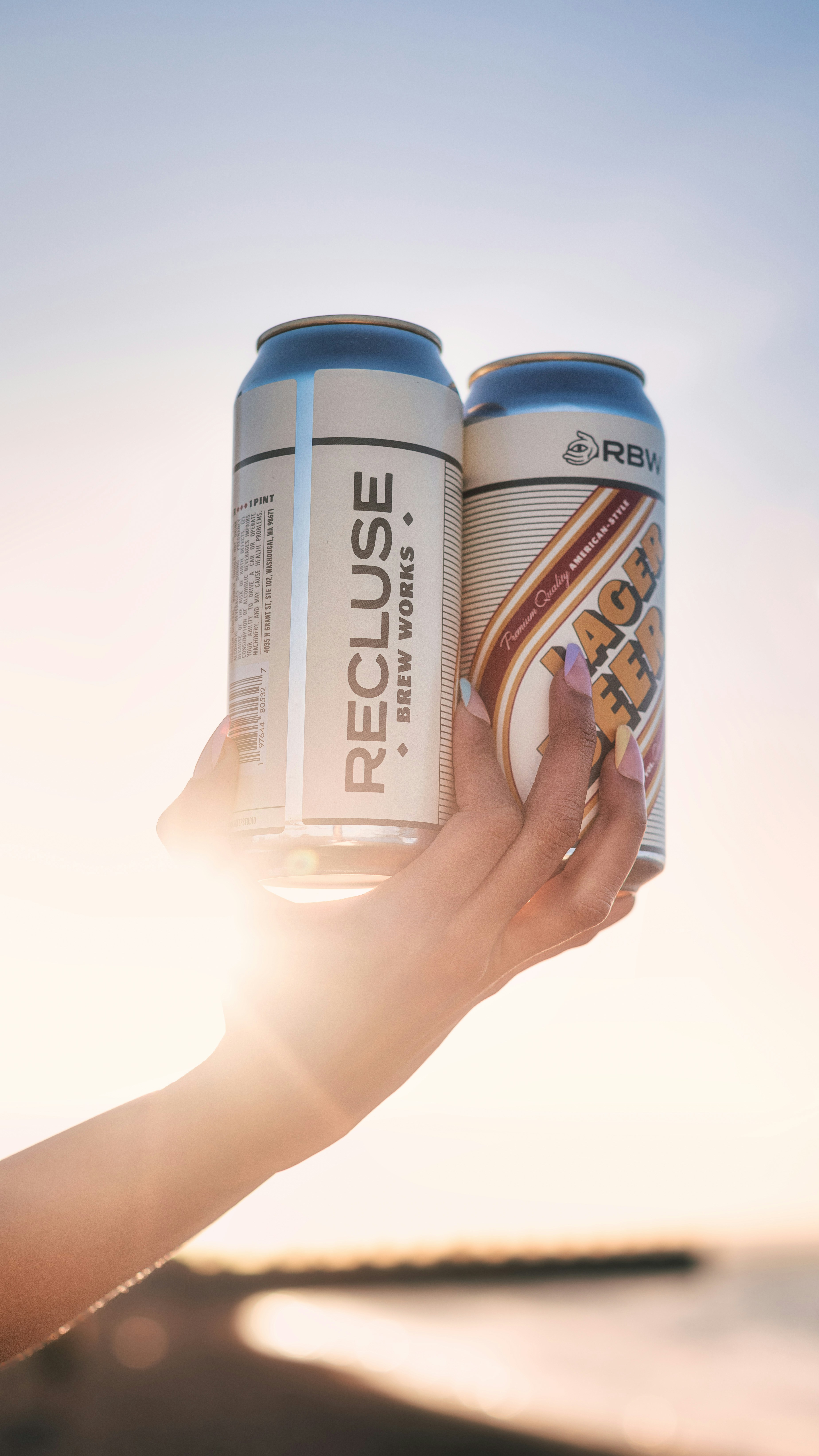 a person holding two cans of beer in their hand