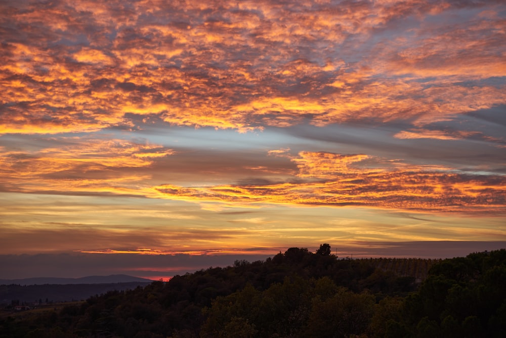 ein Sonnenuntergang mit Wolken und Bäumen im Vordergrund