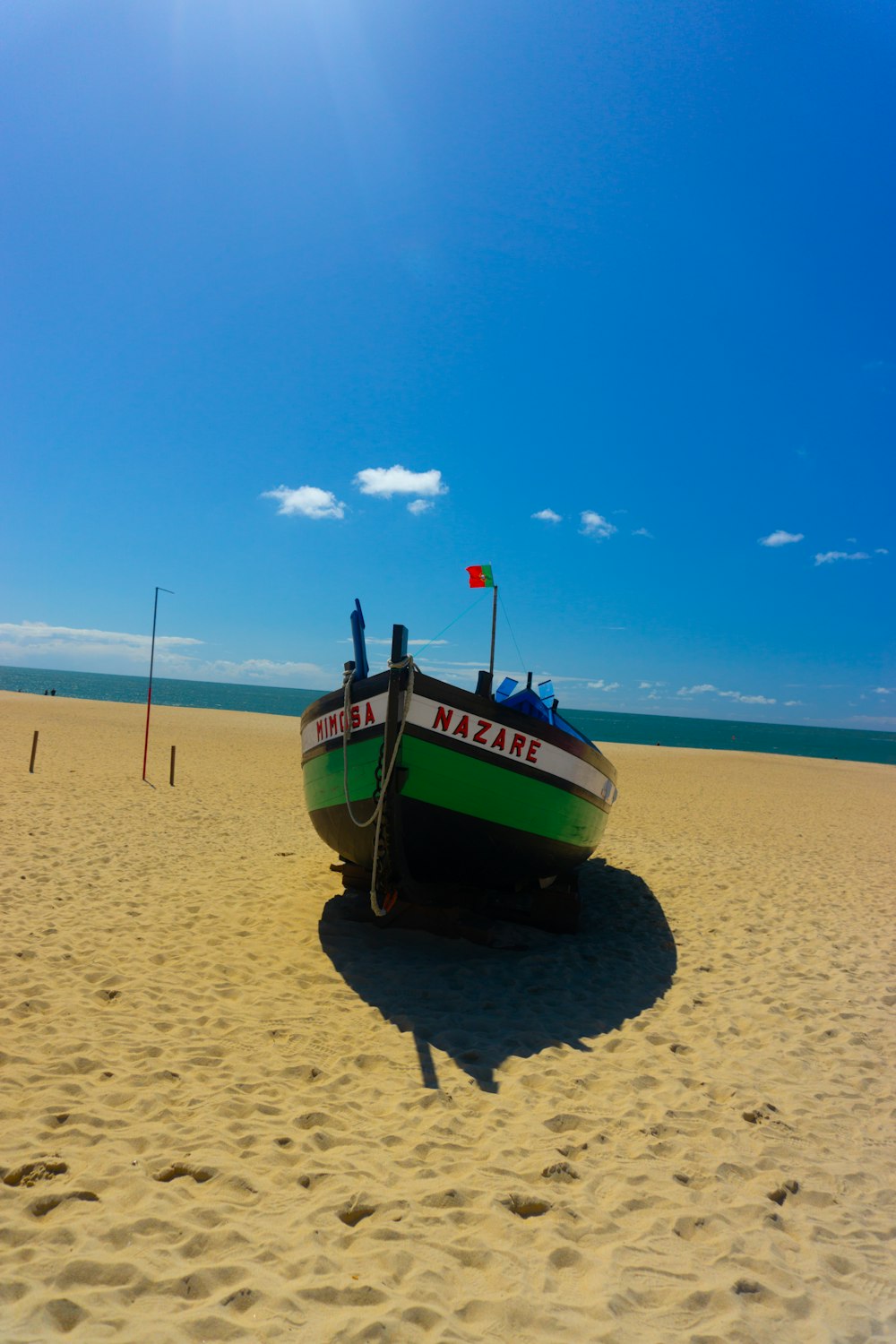 a green and white boat sitting on top of a sandy beach