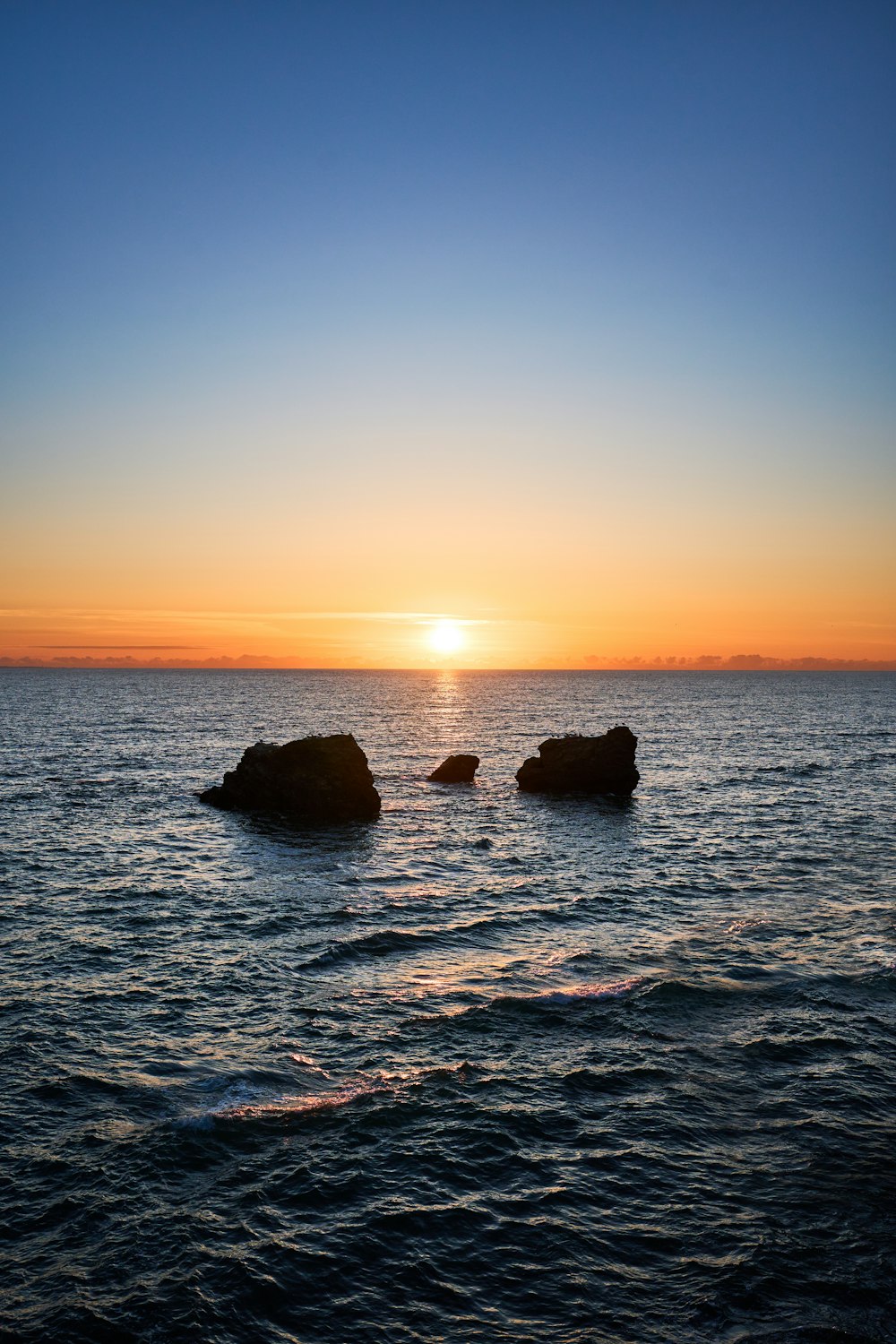 the sun is setting over the ocean with rocks in the water
