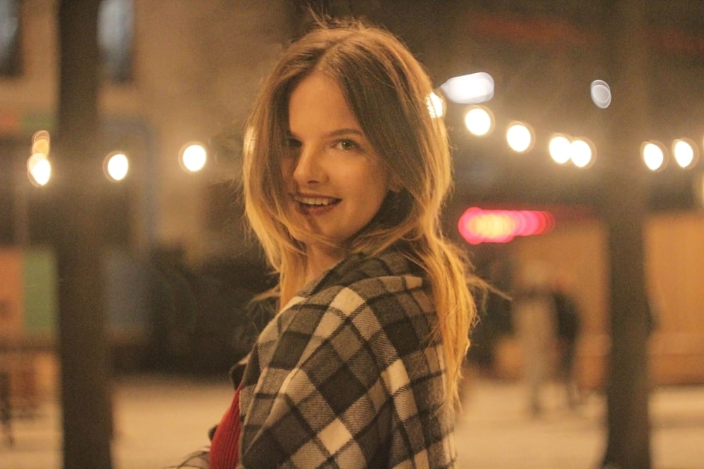 a woman standing on a sidewalk with a plaid coat on