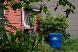 a blue trash can sitting next to a red house