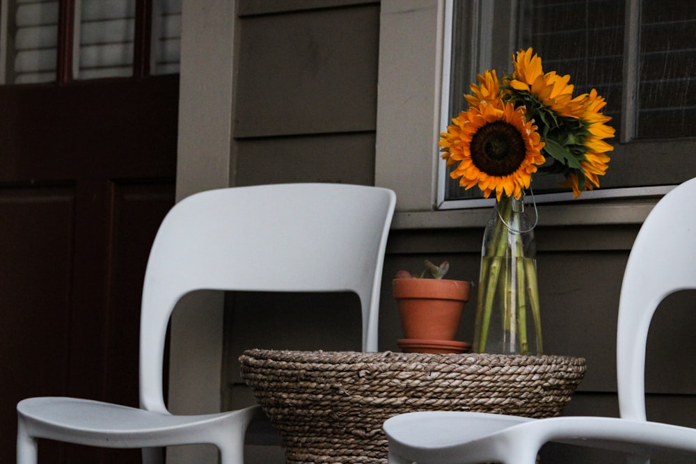 two white chairs and a table with a vase of sunflowers