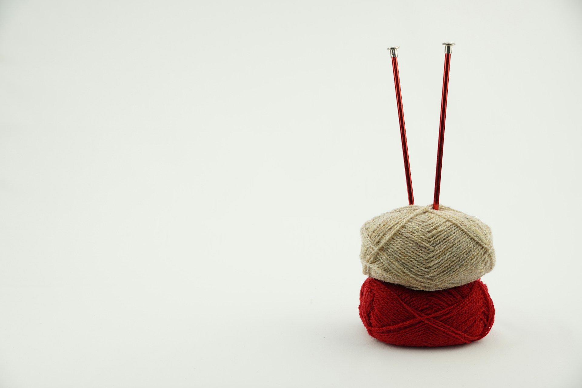 a red ball of yarn and two red knitting needles
