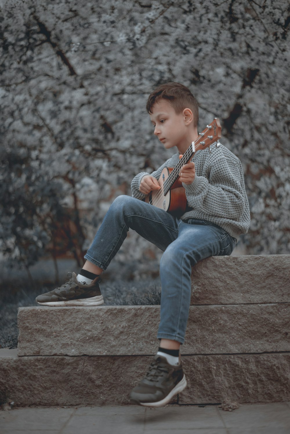 a young boy sitting on a ledge playing a guitar