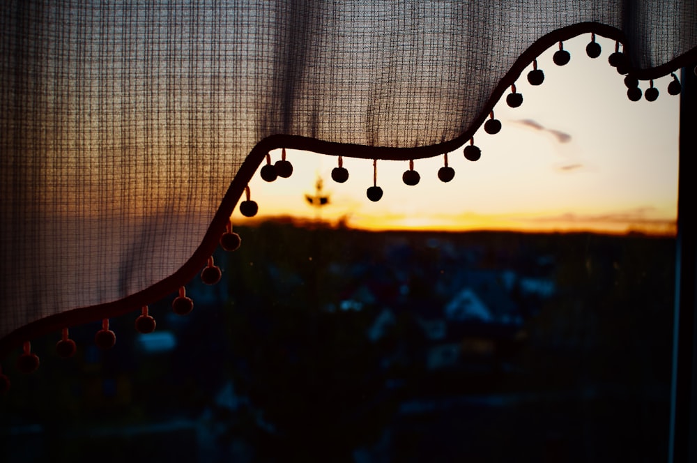 a window with a curtain and a view of a sunset