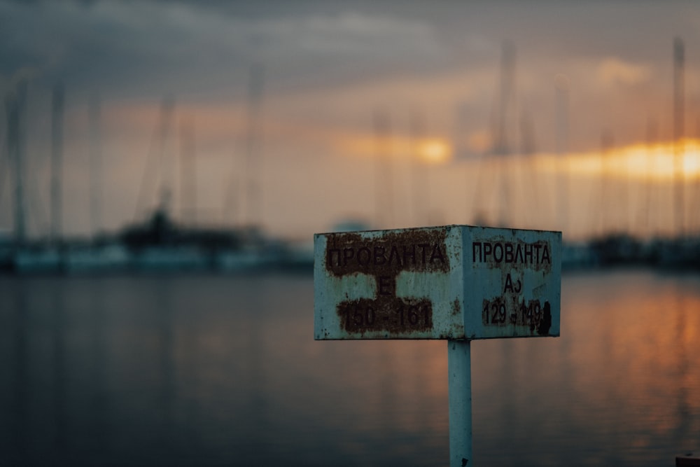 a rusted sign sitting in front of a body of water