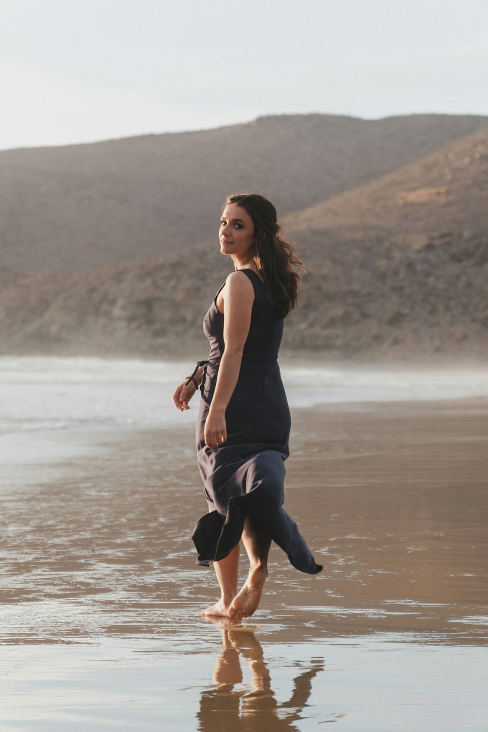 a woman walking on a beach next to the ocean