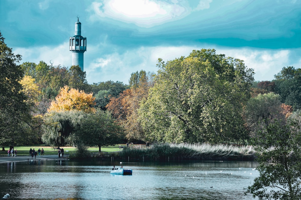 a lake surrounded by trees with a light house in the background