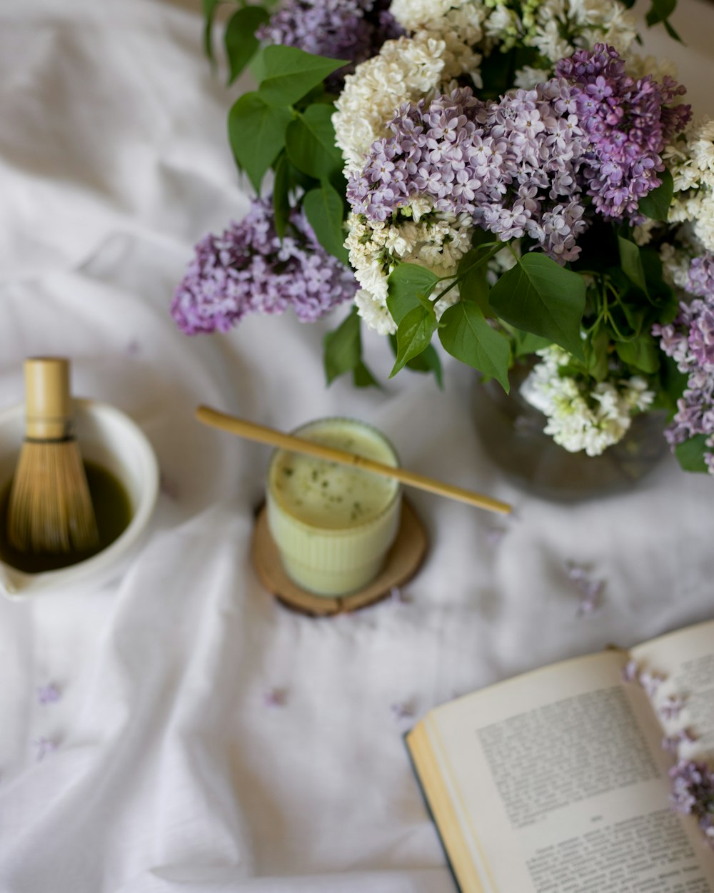 a vase of lilacs and a book on a bed