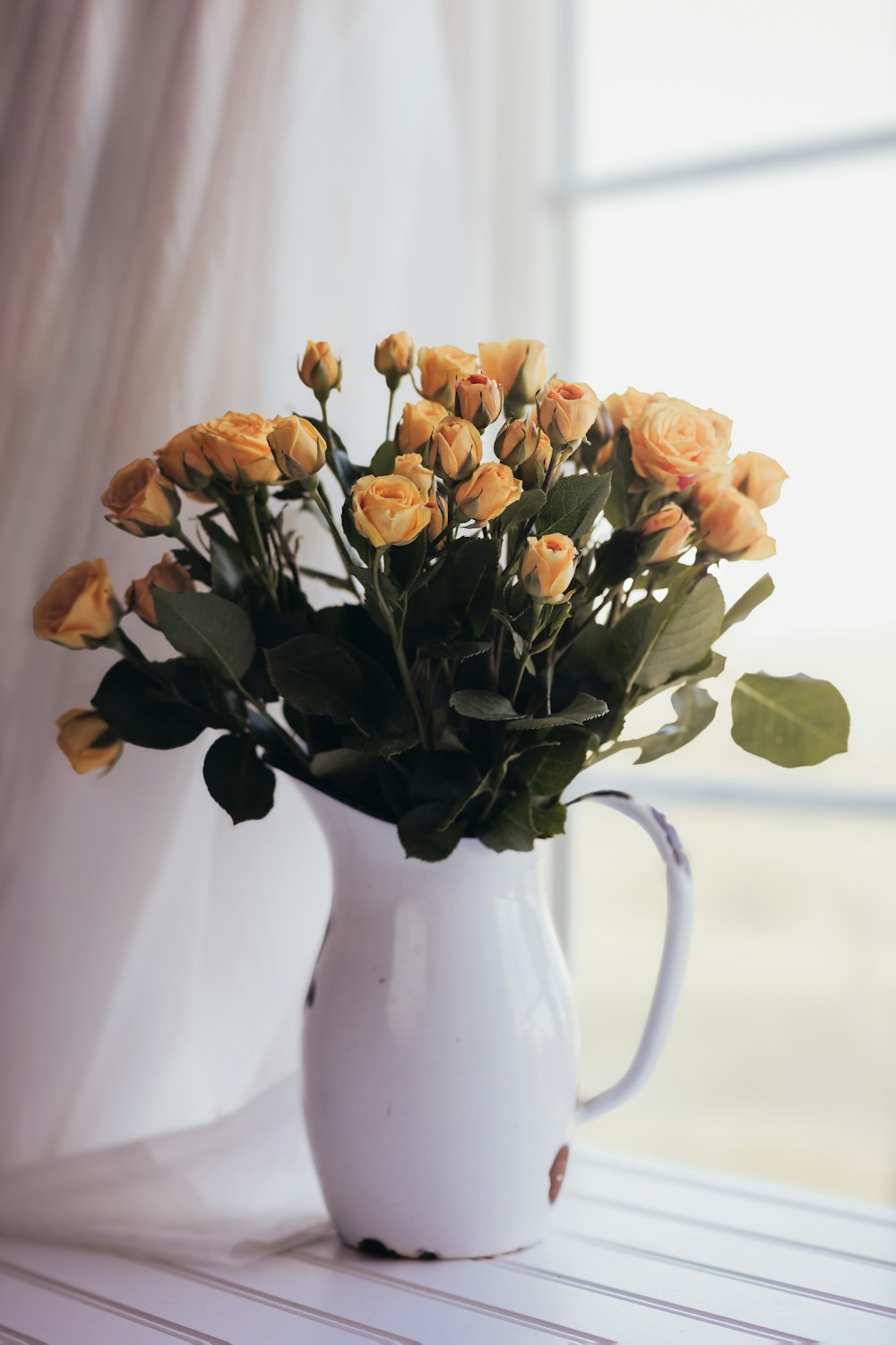 a white pitcher filled with yellow roses on a table