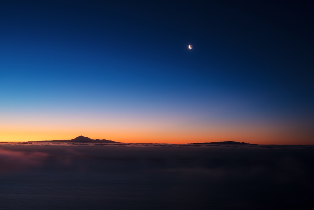 the sun is setting over the mountains and clouds