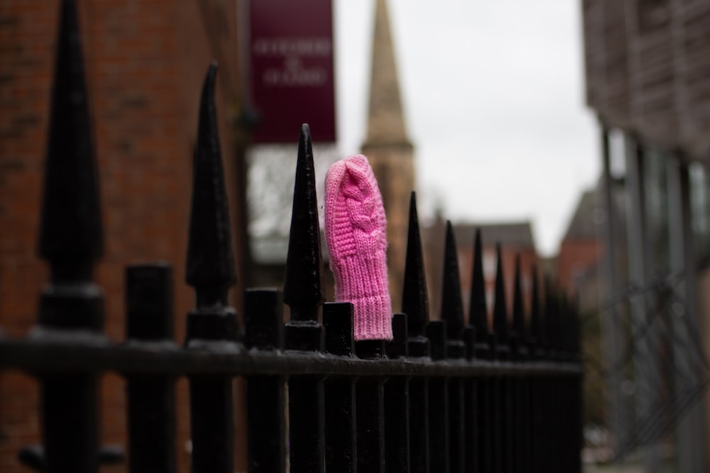a pink knitted mitt sitting on top of a black fence