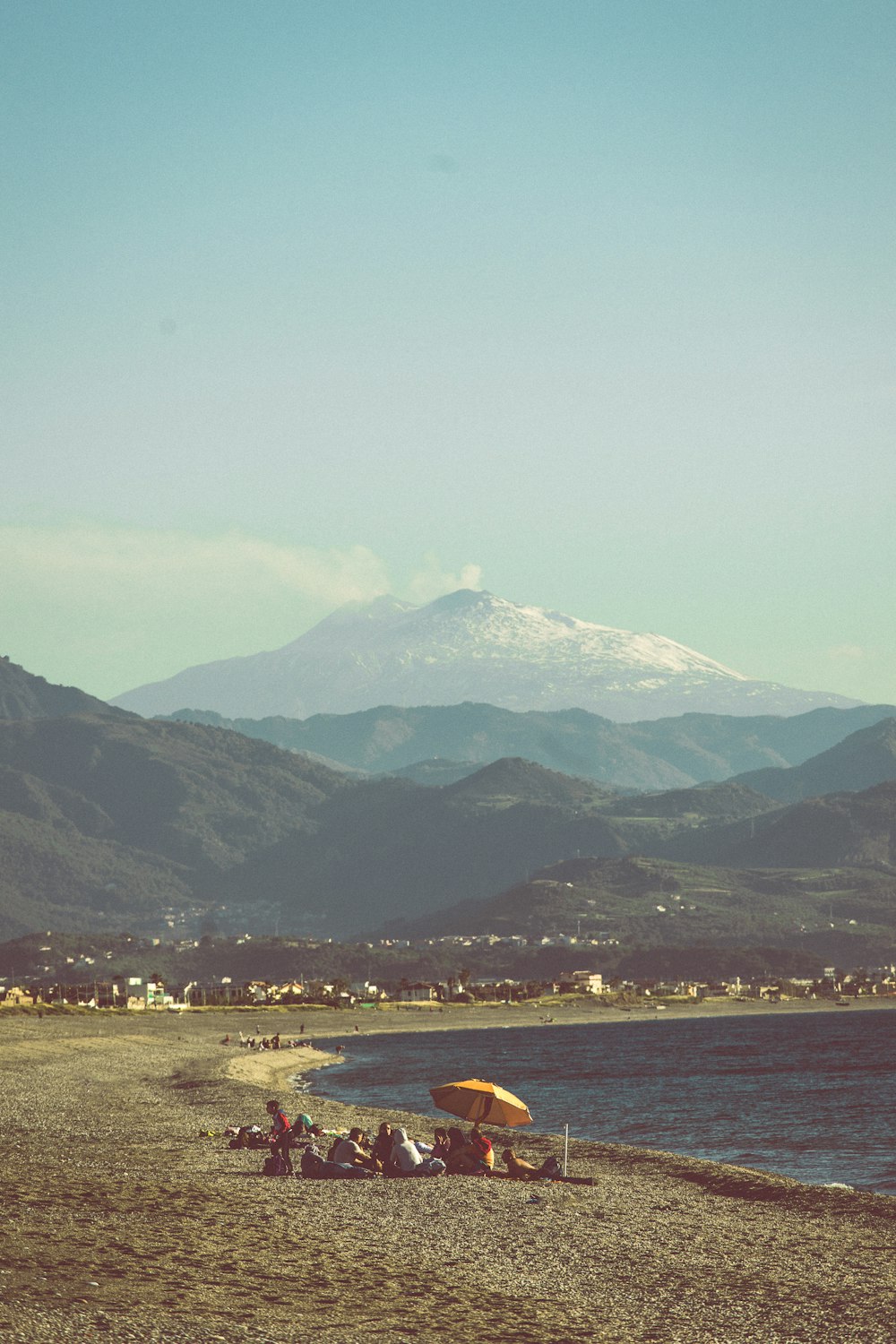 a group of people sitting on a beach next to a body of water