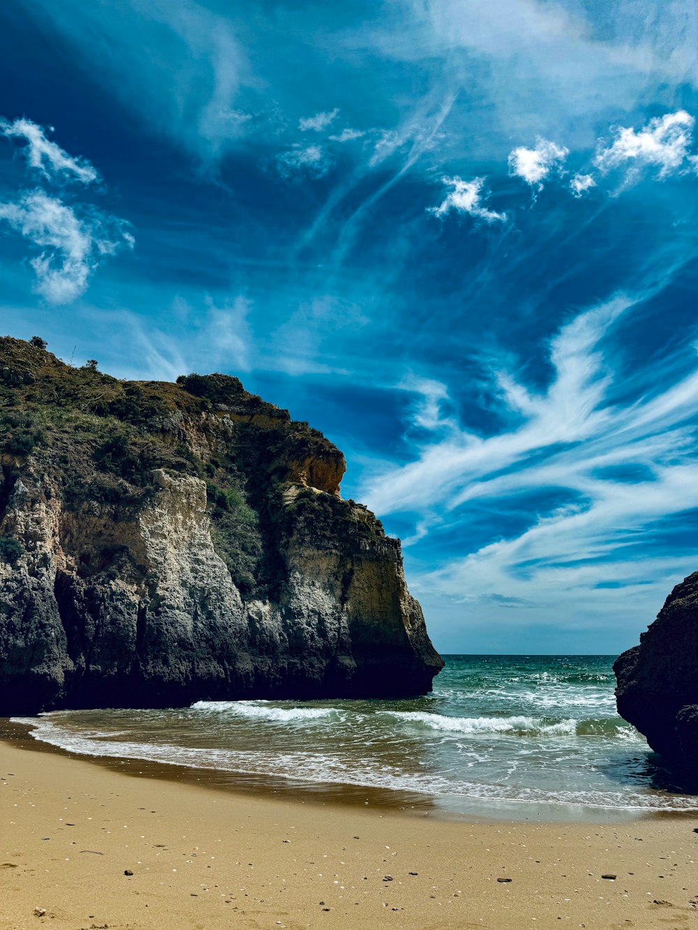 a sandy beach next to a cliff under a blue sky