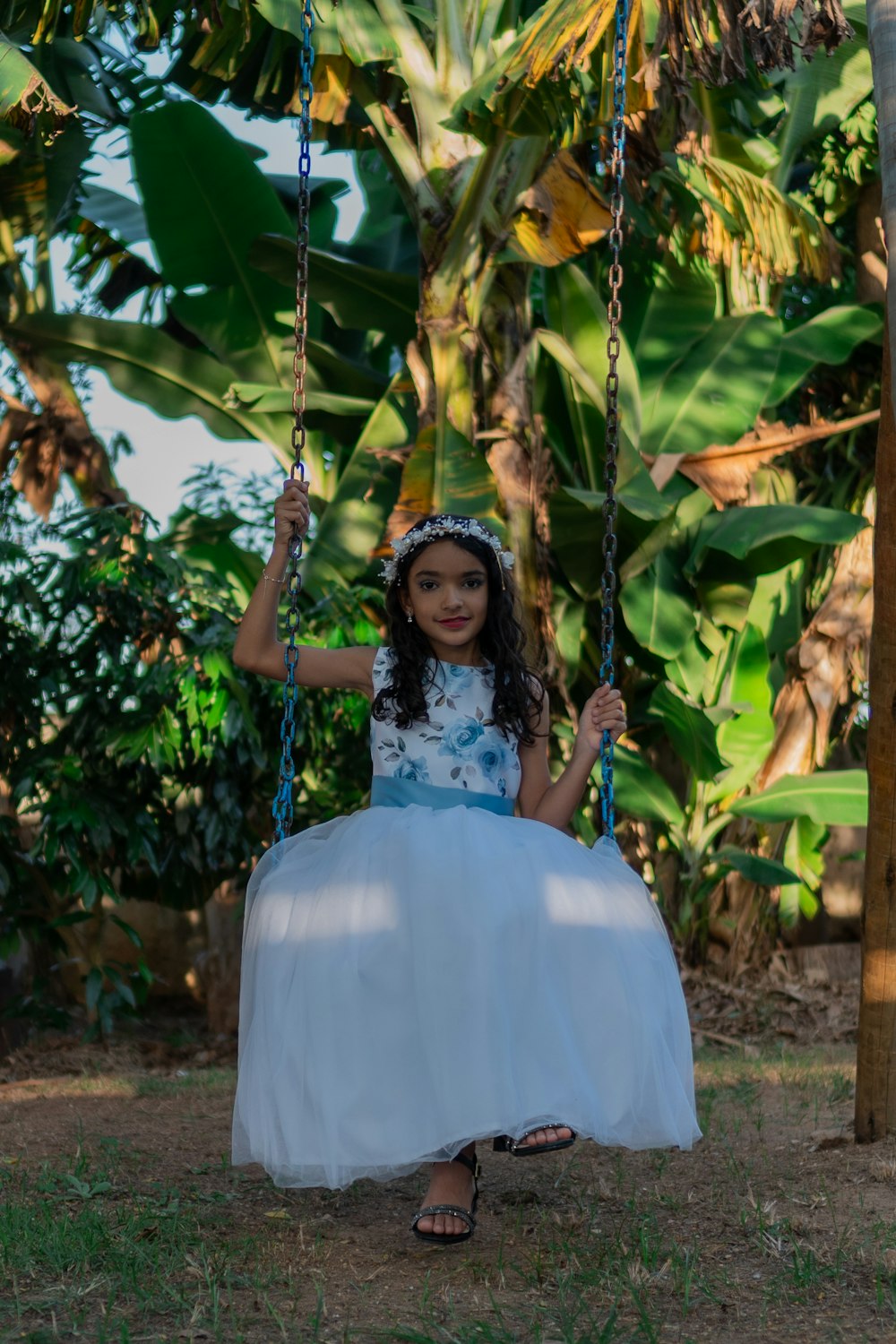 a little girl in a white dress sitting on a swing