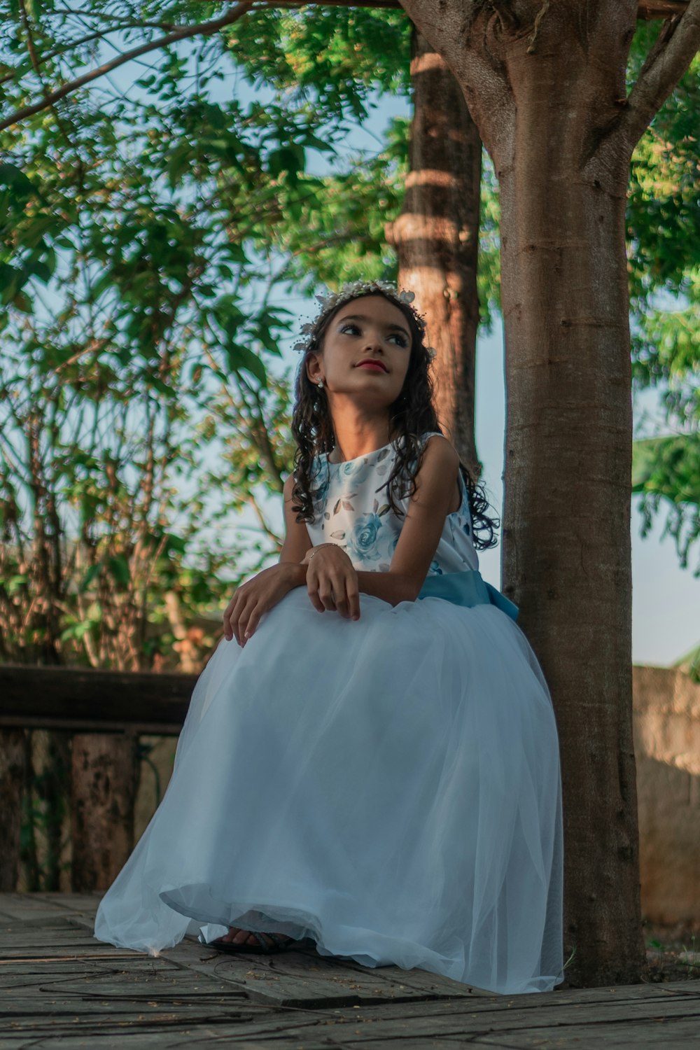 a little girl in a white dress sitting under a tree