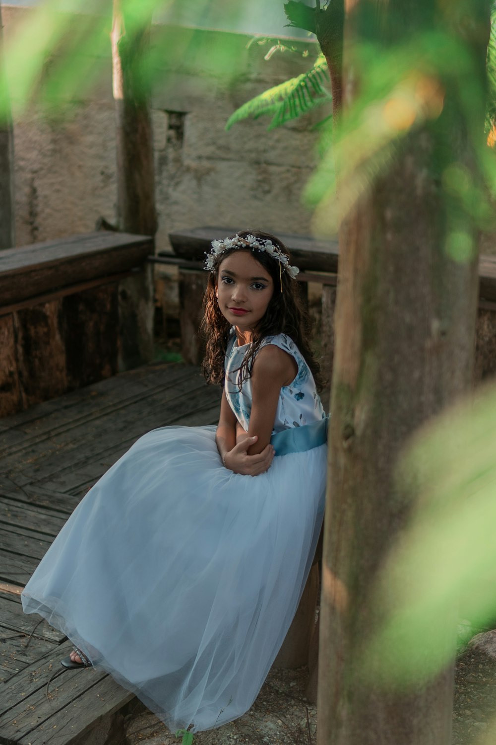 a little girl in a blue dress sitting on a wooden deck