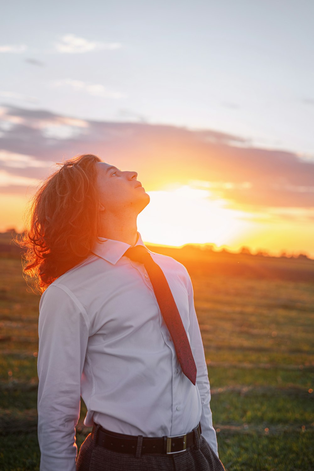 a man standing in a field with the sun setting behind him