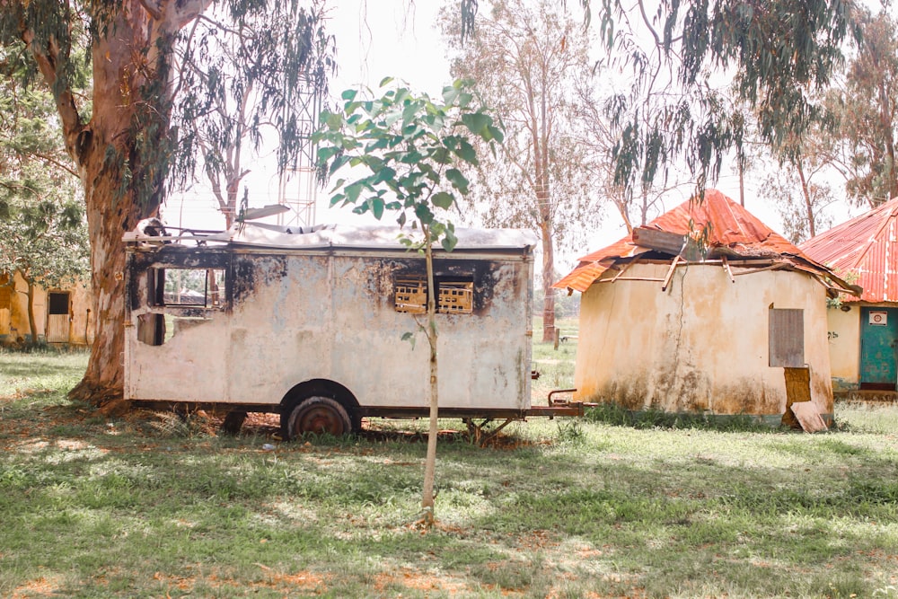 an old trailer parked in a field next to a tree