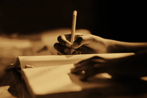 a person holding a pencil and writing in a notebook