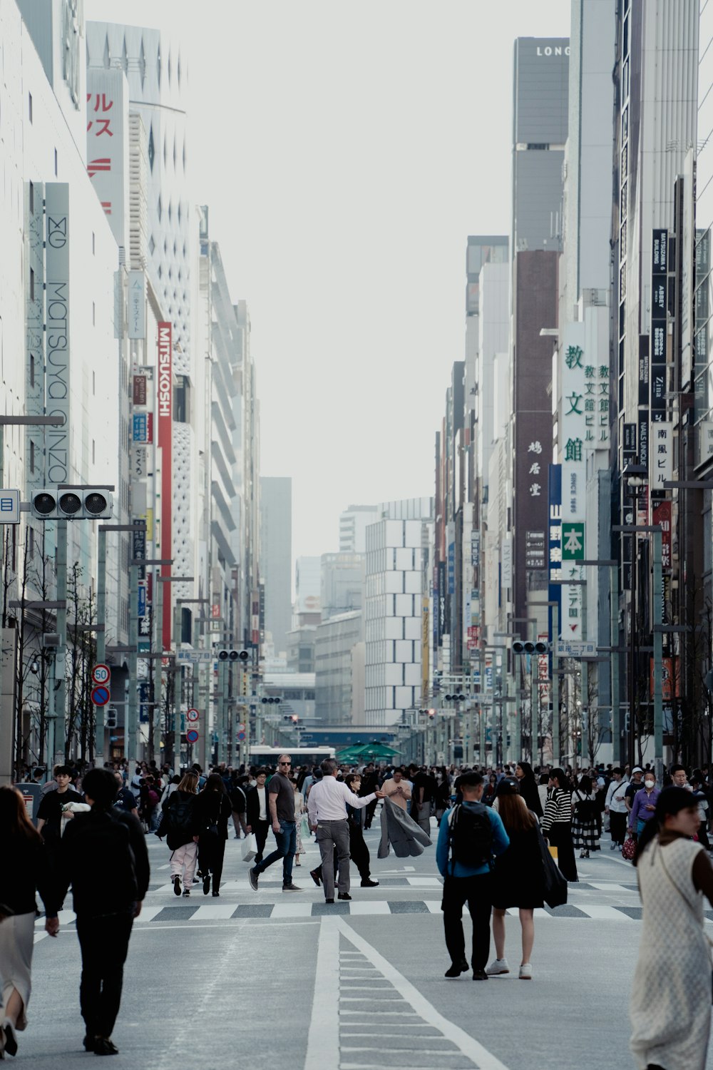 a group of people walking across a street next to tall buildings