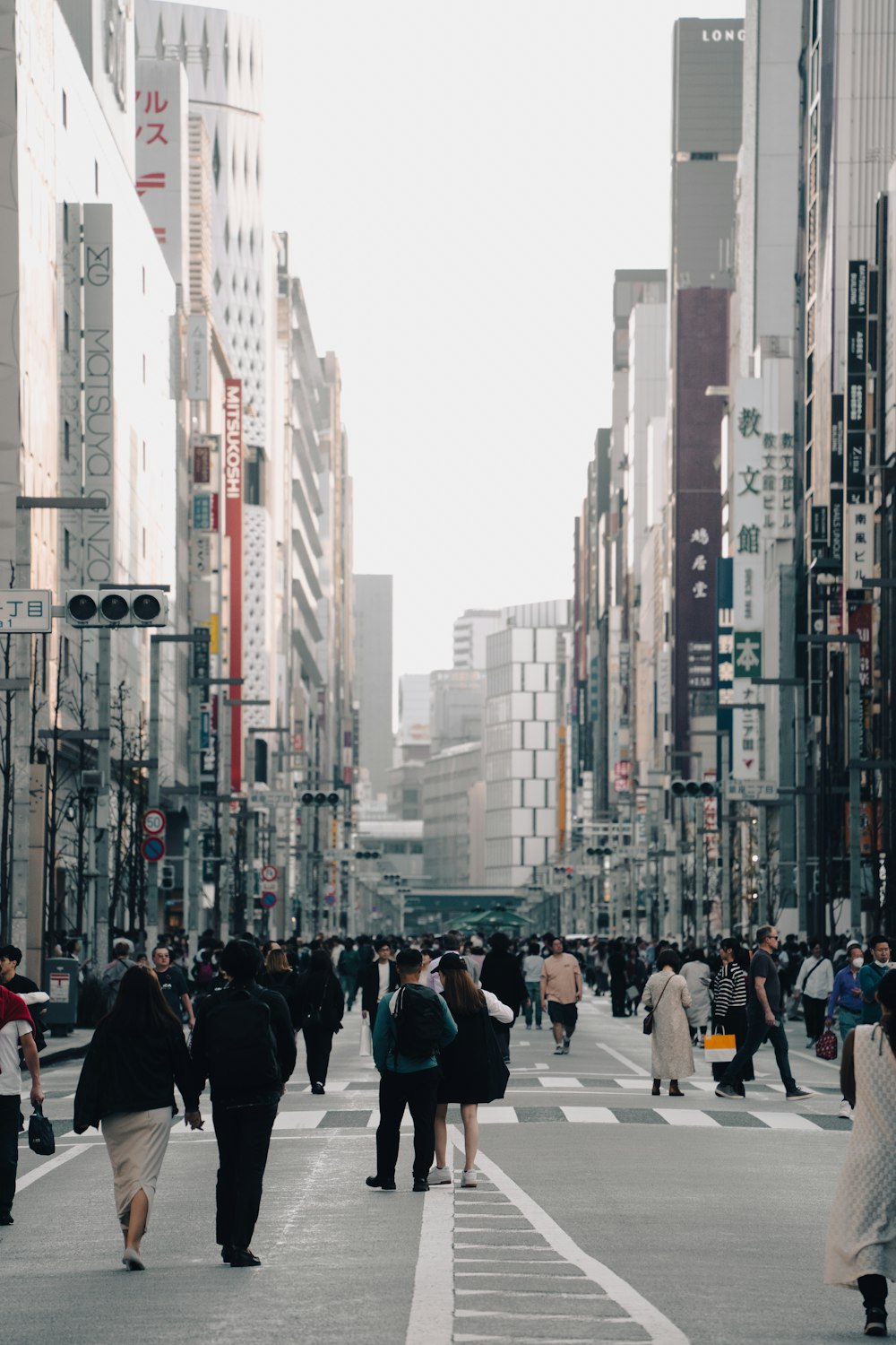 a group of people walking across a street next to tall buildings