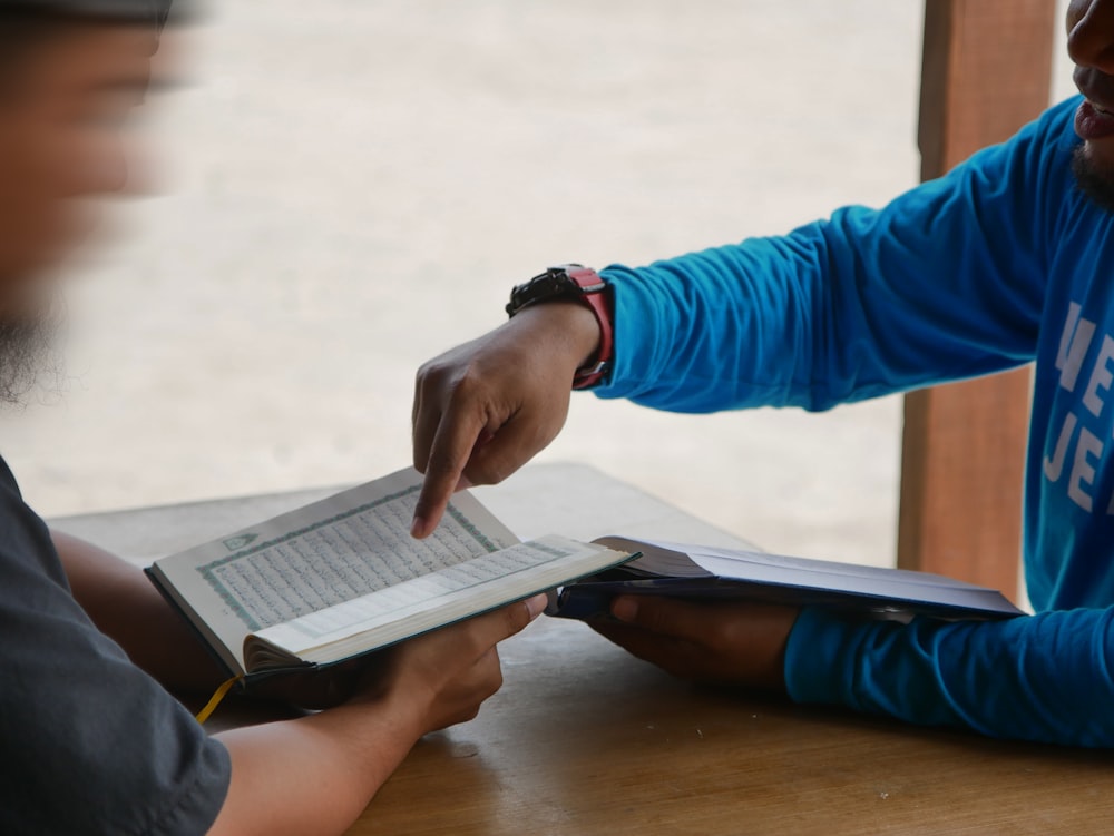 two people sitting at a table with an open book