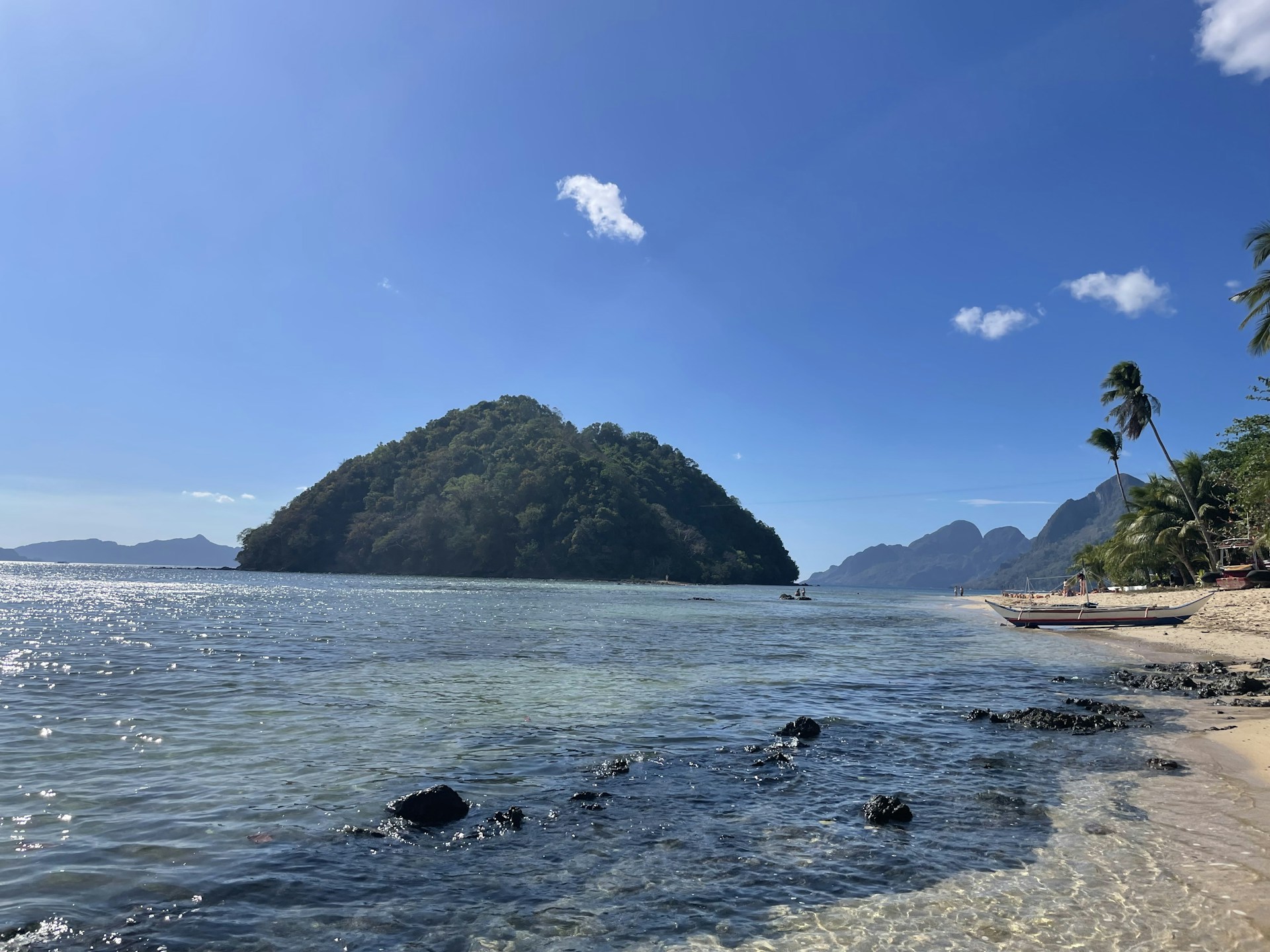 a beach with a boat in the water and a mountain in the background
