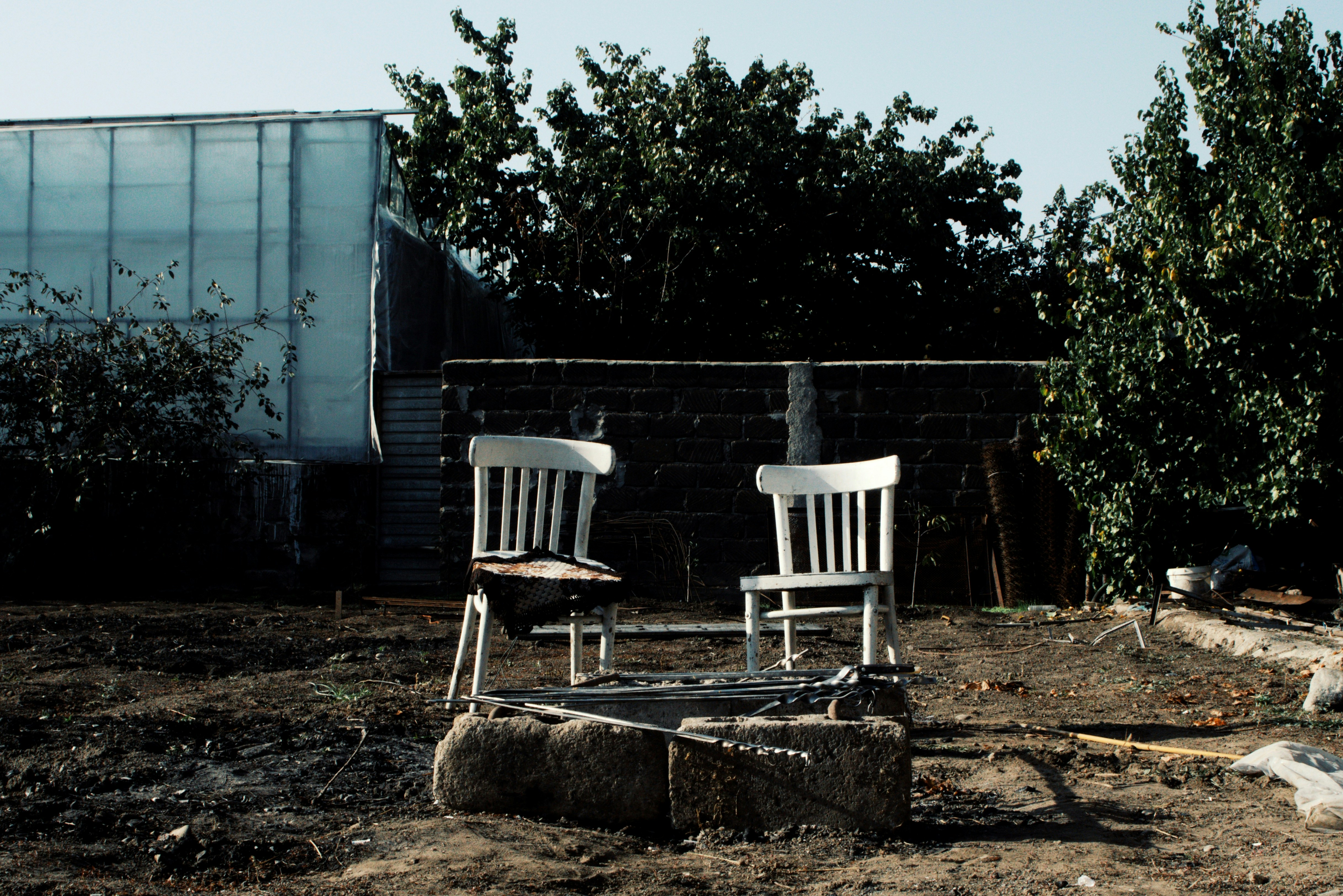 two white chairs sitting on top of a dirt field