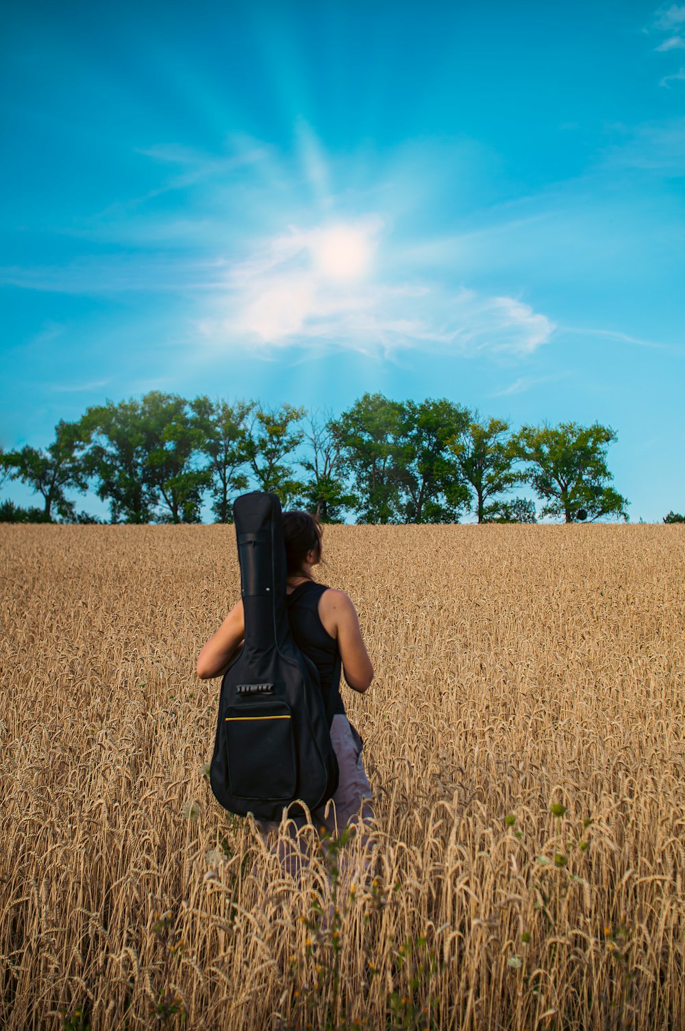 a person standing in a field with a guitar case on their back