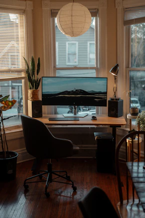 a desk with a computer on it in front of a window