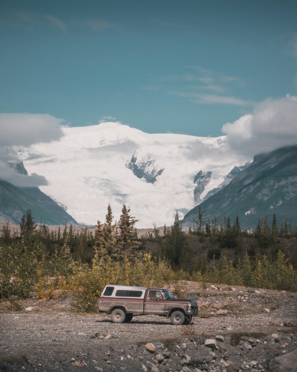 a truck is parked on a gravel road with mountains in the background