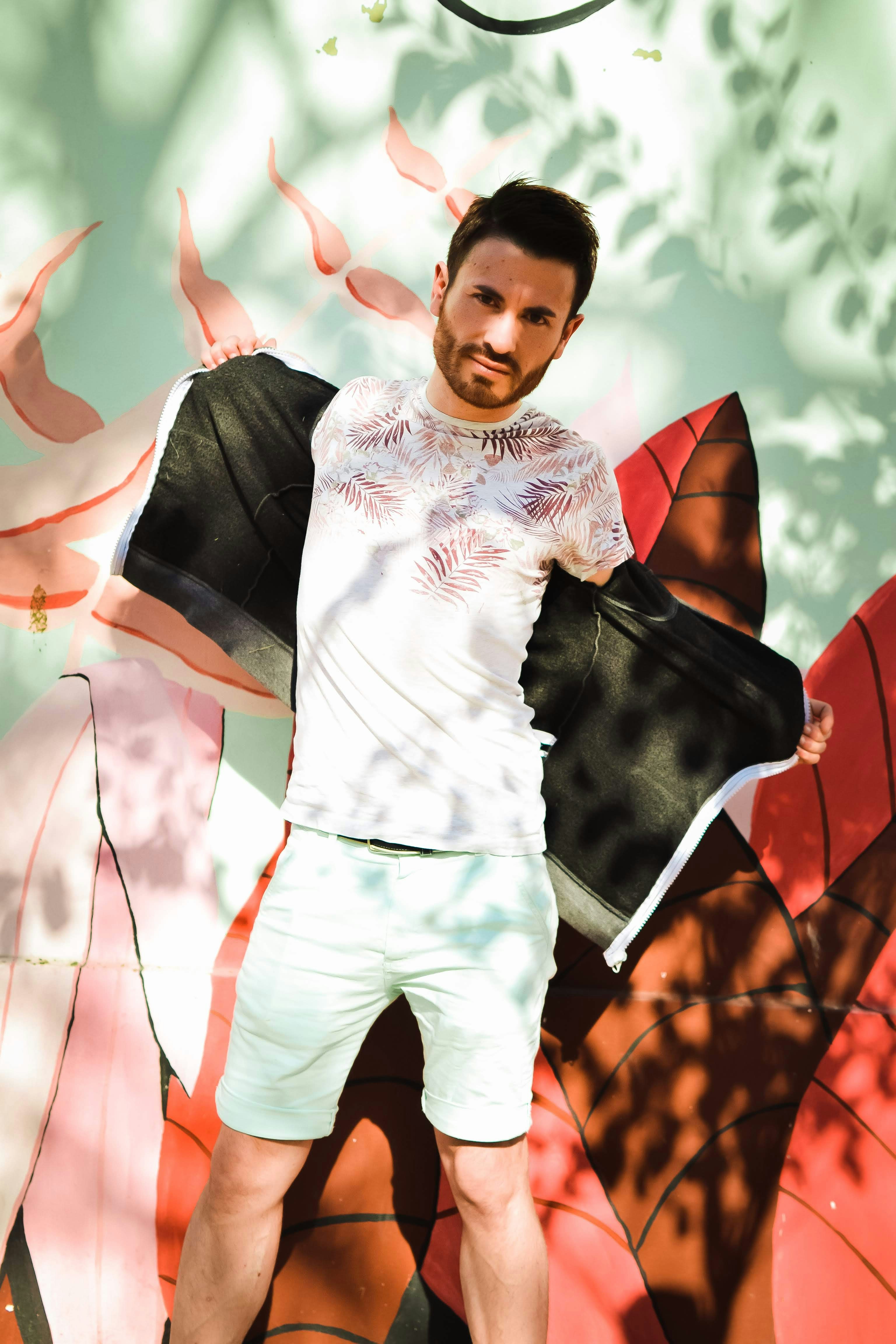 a man in white shirt and white shorts holding a black umbrella