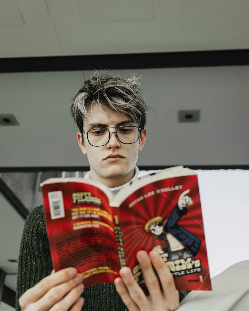 a young man reading a book while wearing glasses