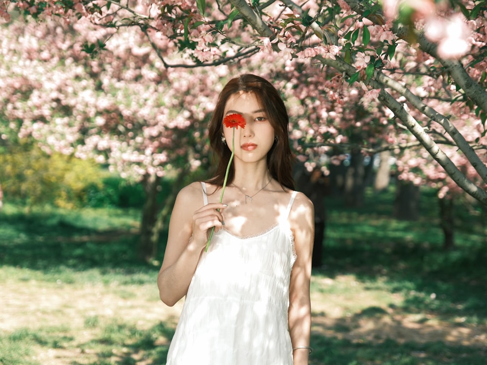 a woman standing under a tree with a flower in her hand