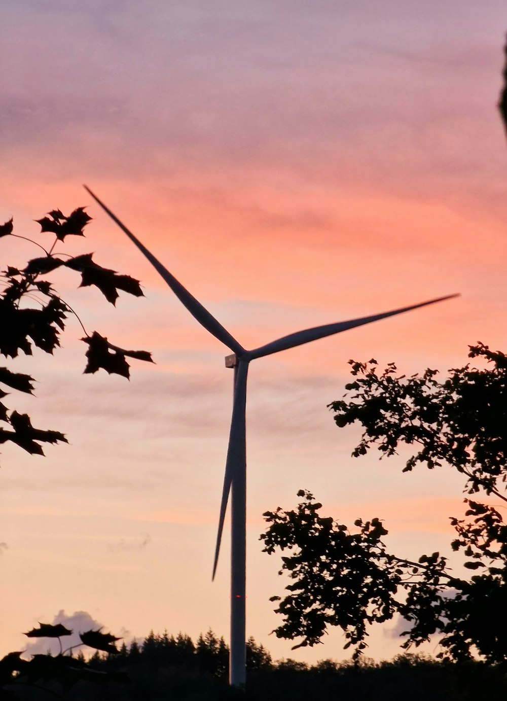 a wind turbine is silhouetted against a pink sky