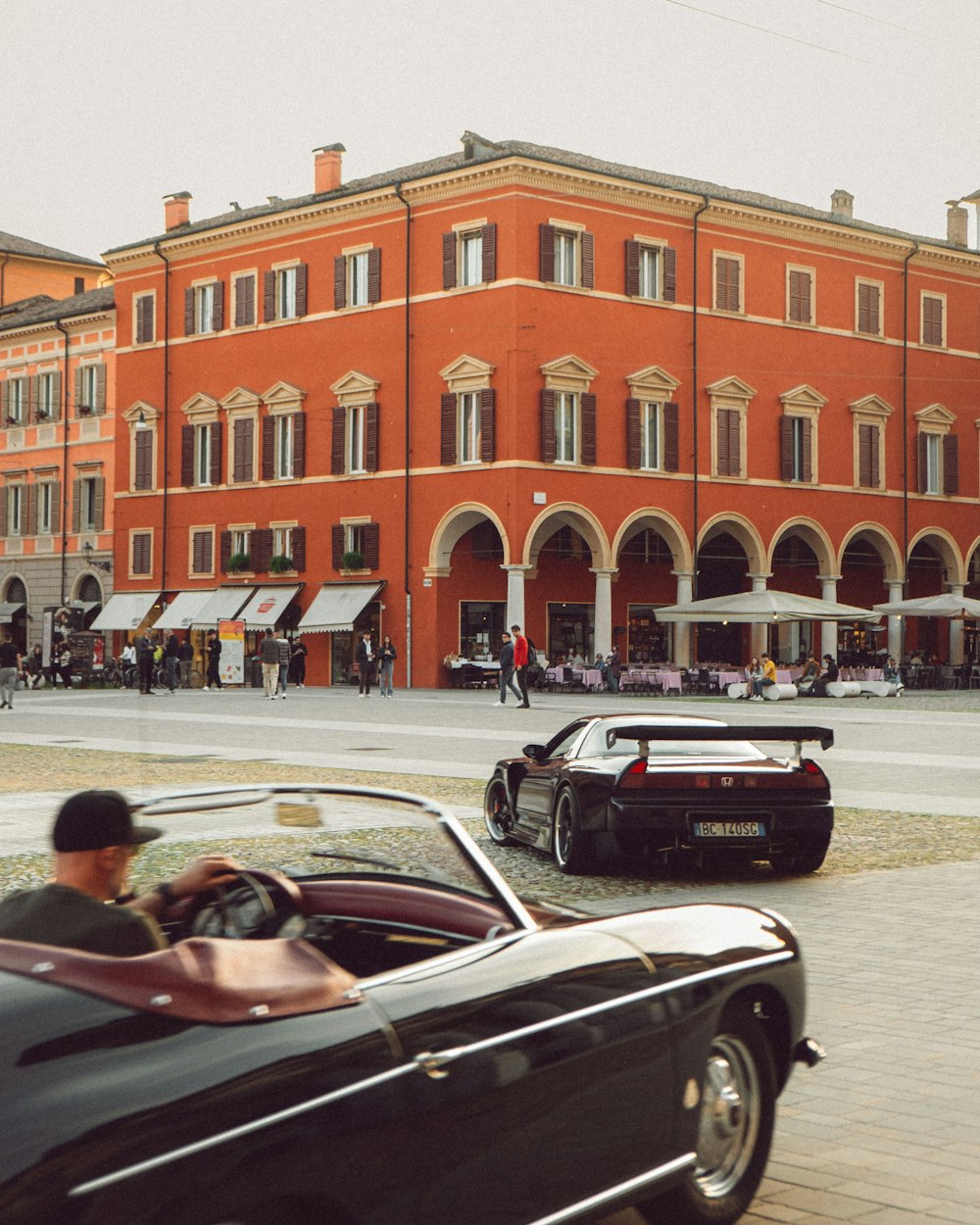 a man driving a black sports car past a red brick building