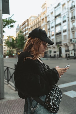 a woman standing on a street corner looking at her cell phone